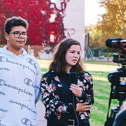 Zwei Jugendliche stehen vor einer Kamera und geben ein Interview