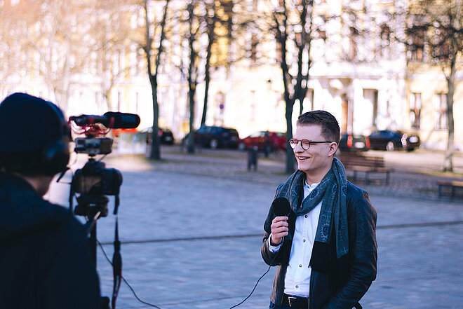 Ein junger Mann mit Mikrofon, der vor einer Kamera steht 