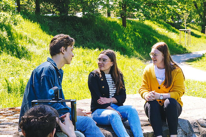 Drei Jugendliche, die zusammen draußen sitzen und reden
